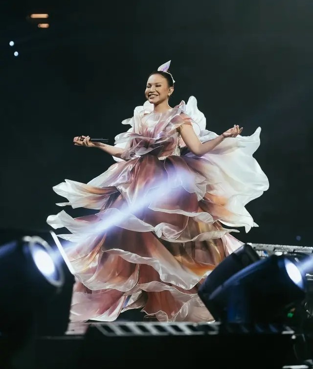 Rossa tampil memukau di atas panggung dengan gaun couture berlayer dramatis berwarna floral yang megah, rambut sleek updo, dan riasan panggung flawless.
