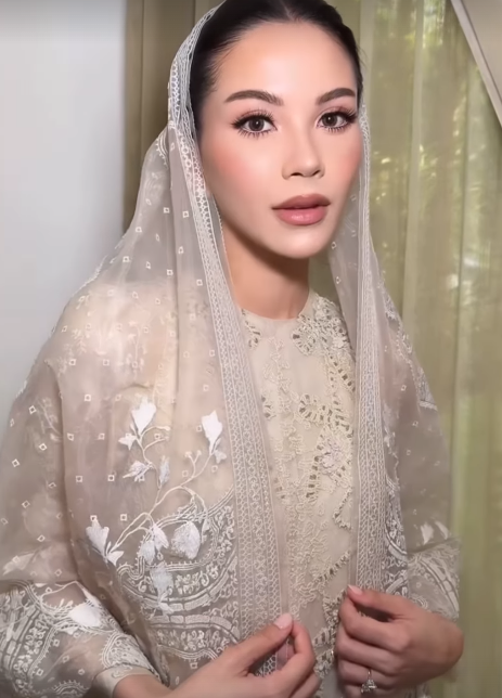 Alyssa Daguise mengenakan kebaya putih berhijab dengan backdrop bunga peach