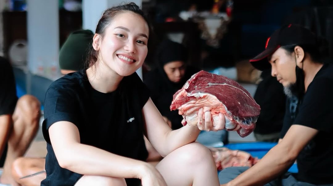 Ayu Ting Ting mengenakan kaos hitam dan celana hijau army saat berpose bersama daging kurban