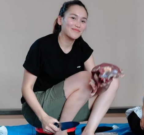 Ayu Ting Ting duduk sambil memegang daging kurban, tampil sederhana dengan outfit casual.