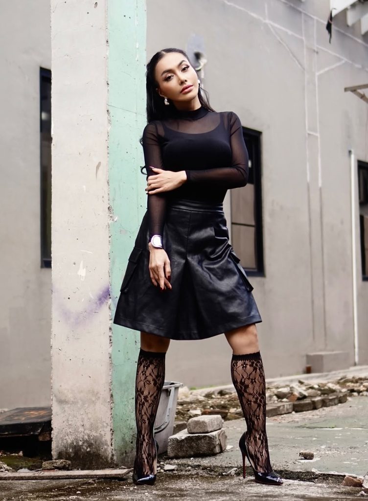 Yang paling mencuri perhatian adalah pilihan aksesori yang tidak biasa: stocking renda hitam dengan motif floral yang menjulur hingga ke lutut.
