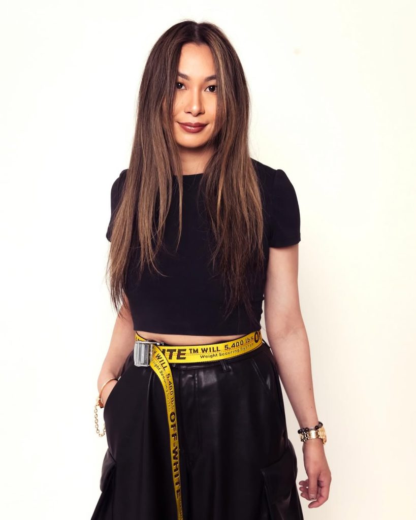 Lucy Guo memakai atasan dan rok hitam dengan sabuk Off-White kuning sebagai statement piece.
