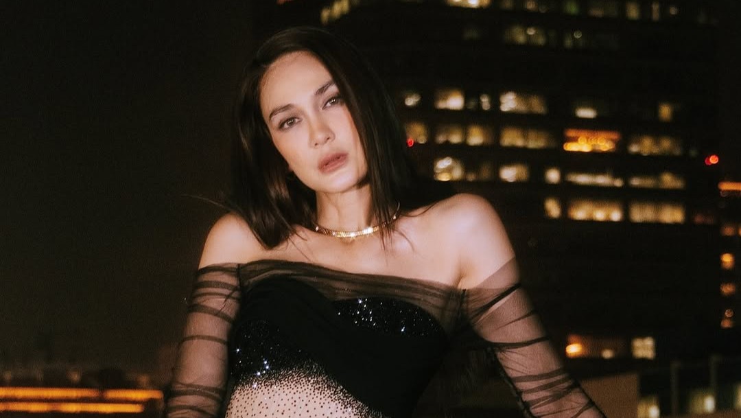 Luna Maya tampil elegan dengan gaun hitam transparan berdiri di balkon menghadap pemandangan kota malam hari