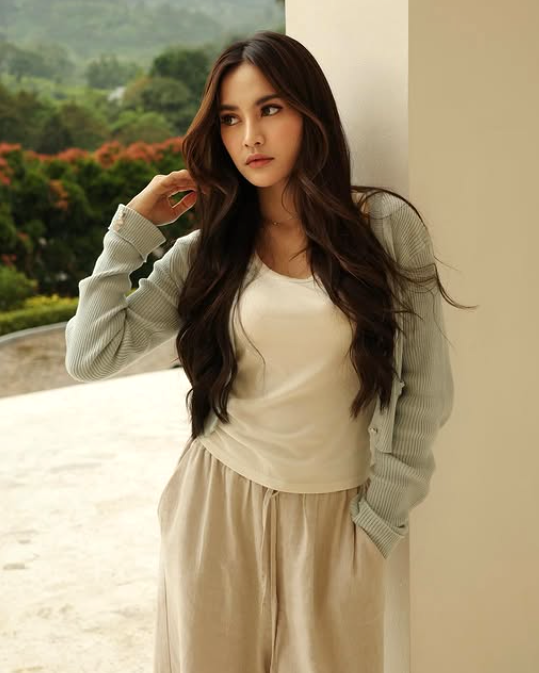 Mahalini mengenakan cardigan sage green dan tank top putih, tampil chic di teras balkon.