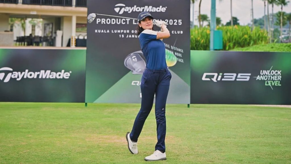 Sigi Wimala melakukan ayunan golf dalam outfit serba navy di acara resmi TaylorMade.