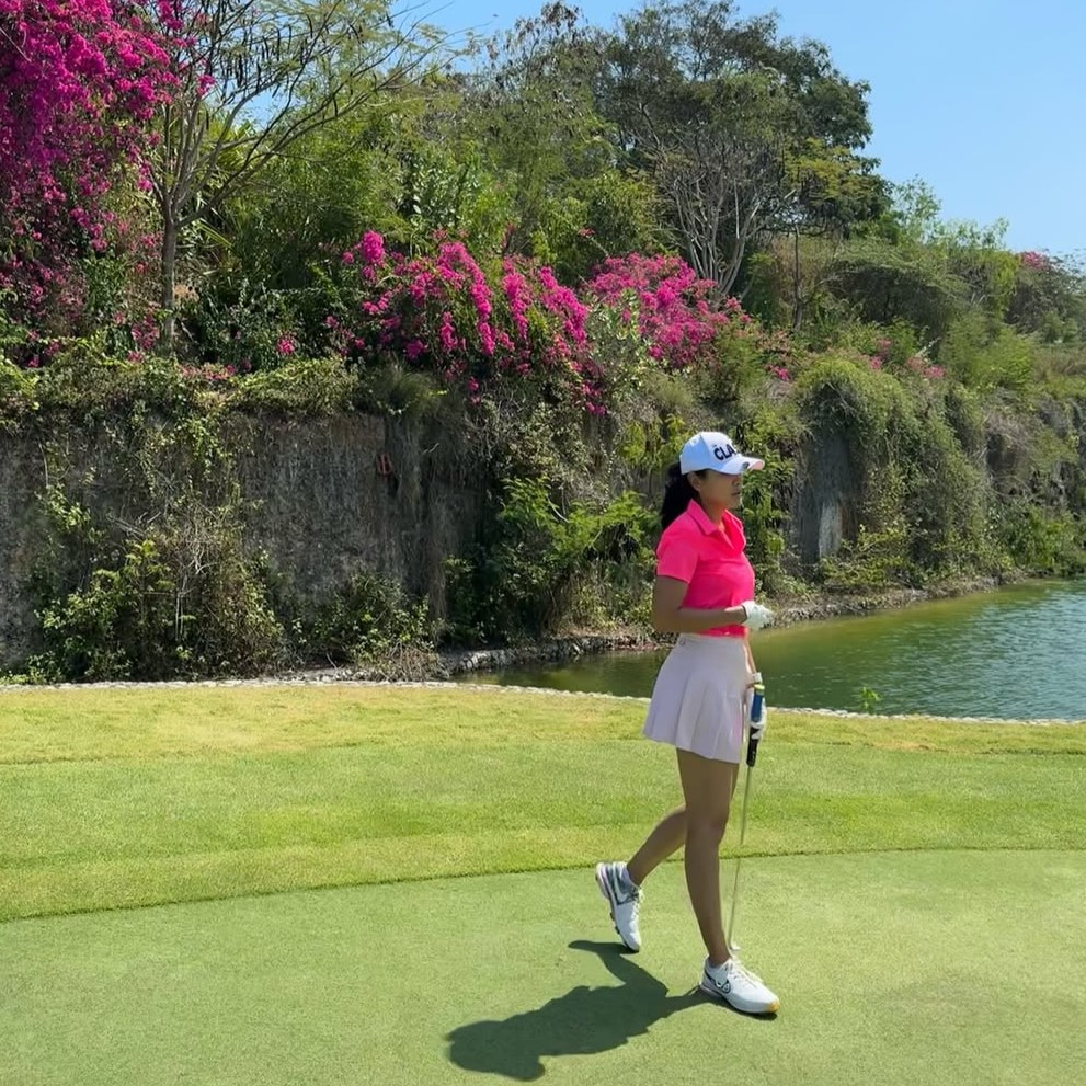 Sigi Wimala tampil feminin dengan atasan pink dan rok putih di lapangan golf.