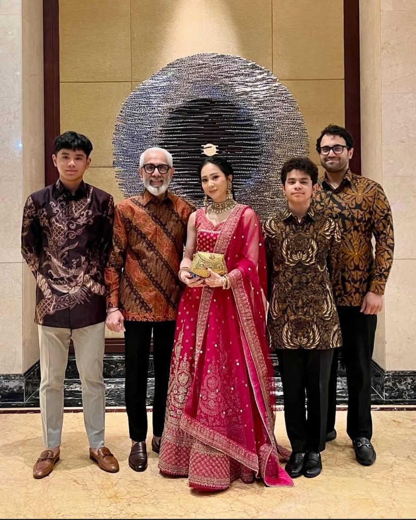Tangan Bunga Zainal dihiasi henna putih bermotif floral dan gelang bertumpuk, difoto close-up saat ia tersenyum di tengah resepsi, menampilkan detail feminin dan etnik yang memikat.