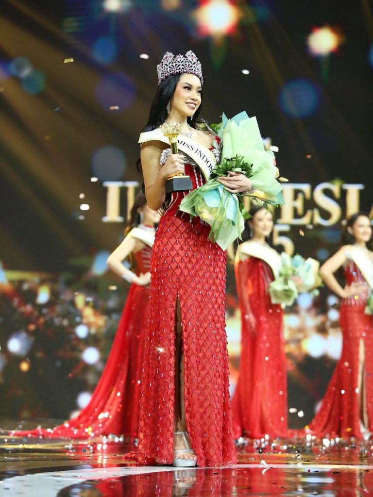 Audrey Bianca mengenakan mahkota Miss Indonesia 2025, tersenyum di atas panggung saat penobatan dengan latar logo dan cahaya megah.