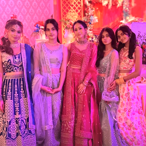 Bunga Zainal mengenakan lehenga merah keunguan dengan bordiran emas, berdiri anggun di ballroom pernikahan, memperlihatkan gaya elegan khas India yang memesona.