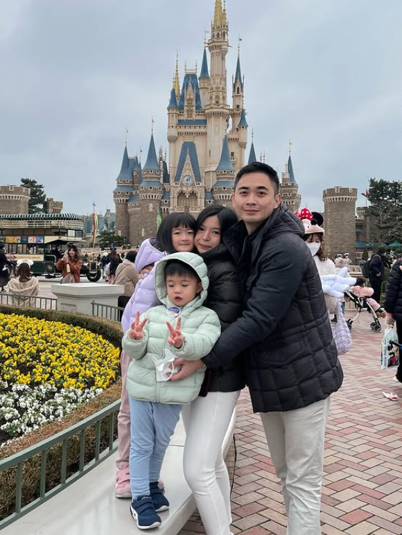 Cindy dan keluarga liburan ke Disneyland berfoto depan kastil ikonik.