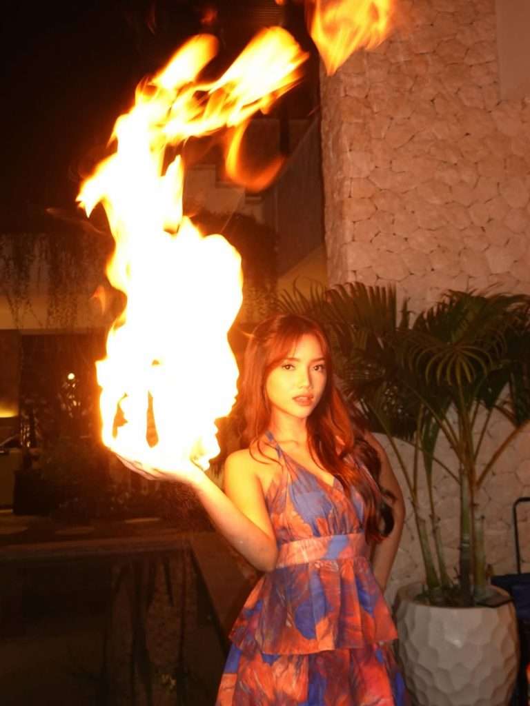 Fuji An mengenakan gaun biru dengan efek api menyala di tangan, tampil seperti Dewi Api