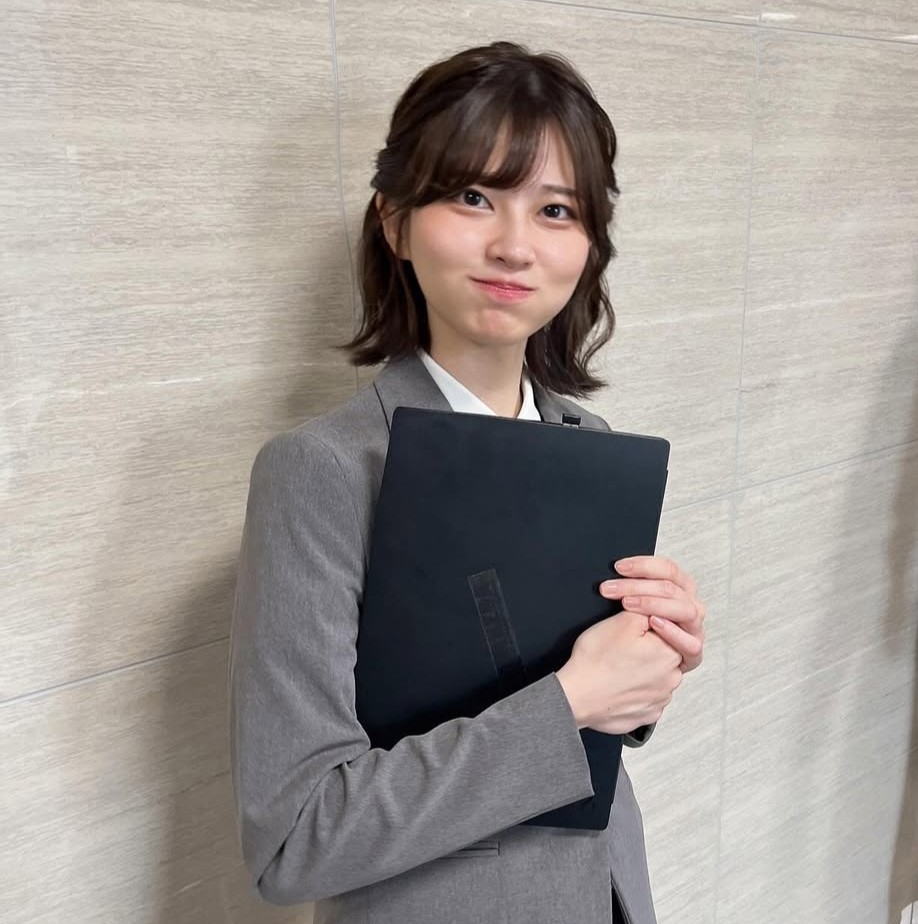 Saori Araki mengenakan jas abu-abu dan memegang laptop, tersenyum dengan pipi mengembung dalam foto viral bertema “Selamat Pagi”.