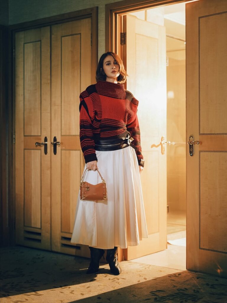 Luna Maya tampil anggun dalam balutan sweater rajut tebal berwarna merah dan hitam, perpaduan warna bold yang memberi kesan hangat sekaligus berani.