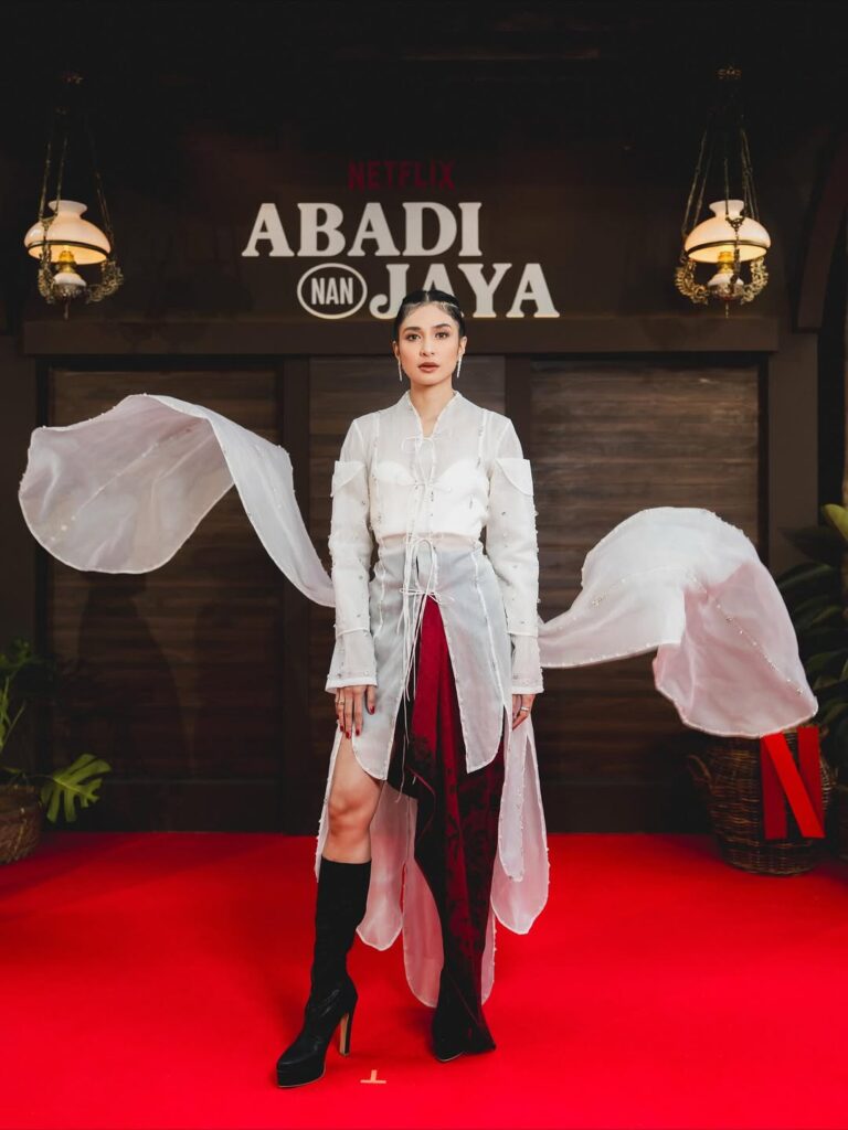 Mikha Tambayong tampil anggun di gala premiere Abadi Nan Jaya dengan busana putih transparan dan kain merah elegan di karpet merah.