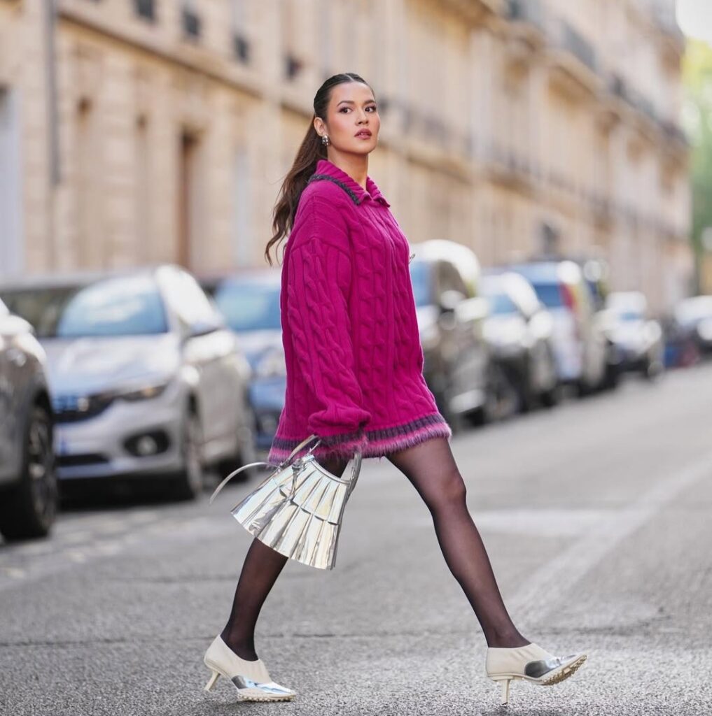 Raisa mengenakan sweater fuchsia oversized dengan pantyhose hitam dan heels putih metalik.
