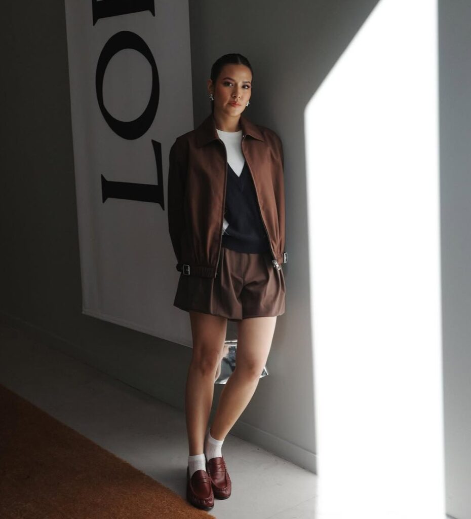 Raisa mengenakan setelan cokelat dengan celana pendek dan loafers merah marun.