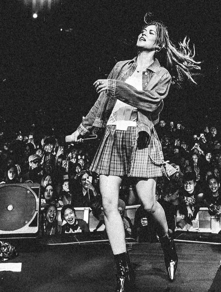 Raisa menari di atas panggung dengan rok kotak-kotak dan jaket denim bergaya rock chic.