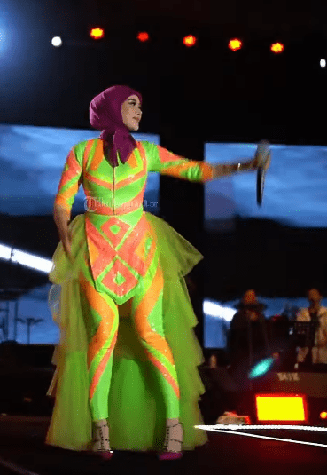 Sepatu stiletto ungu yang dikenakan melengkapi keseluruhan penampilan, menambah kesan glamor sekaligus edgy.