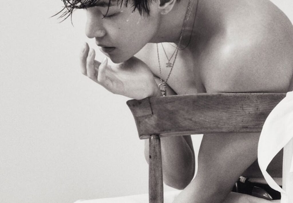 Dalam salah satu foto, V tampak bersandar di kursi tanpa atasan, memperlihatkan bahu lebar dan otot lengannya. 